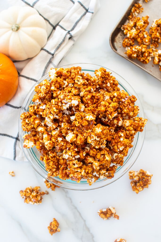 homemade caramel corn in a glass bowl on a marble counter with pumpkins.
