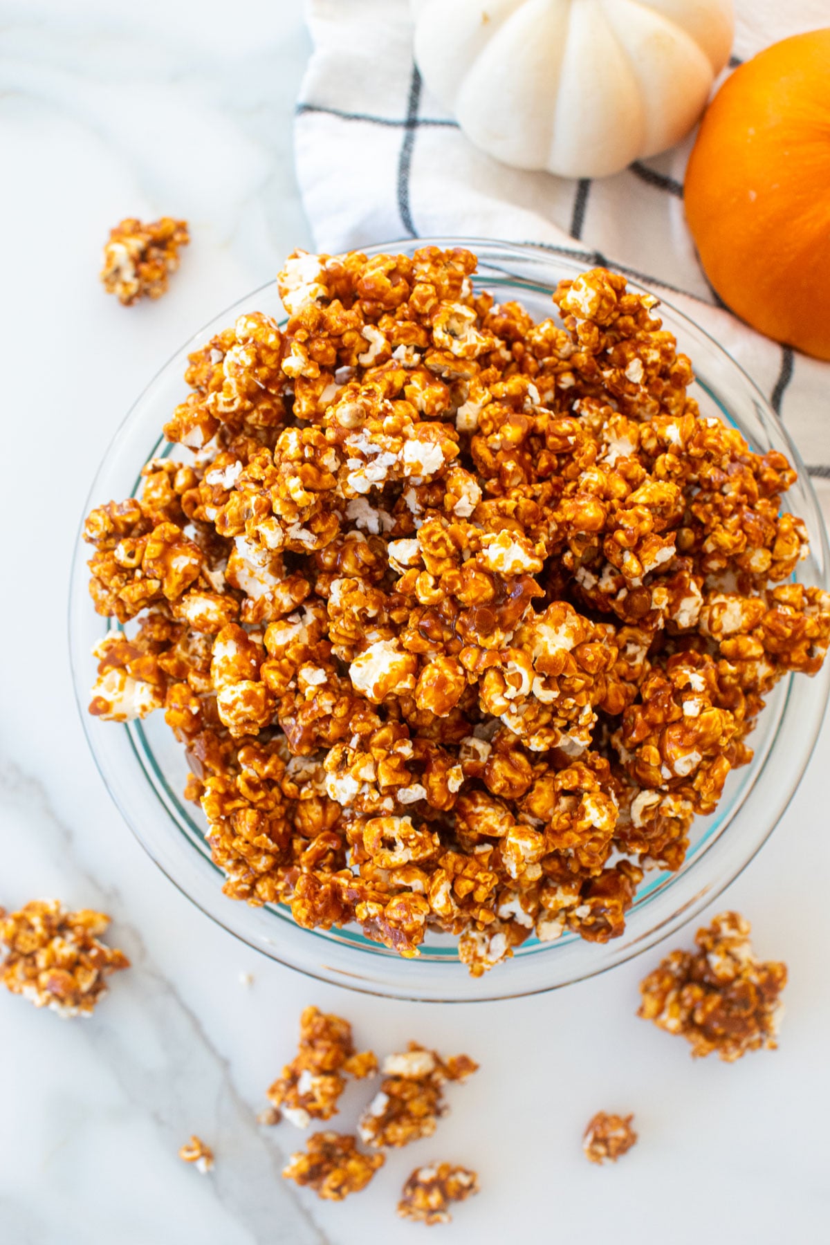 homemade caramel corn in a glass bowl on a marble counter with pumpkins.
