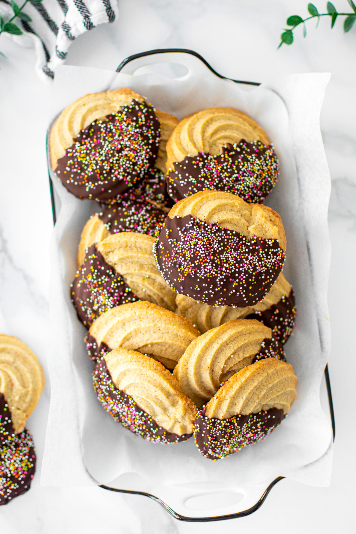 dark chocolate dipped butter cookies with naturally colored rainbow sprinkles on a platter.