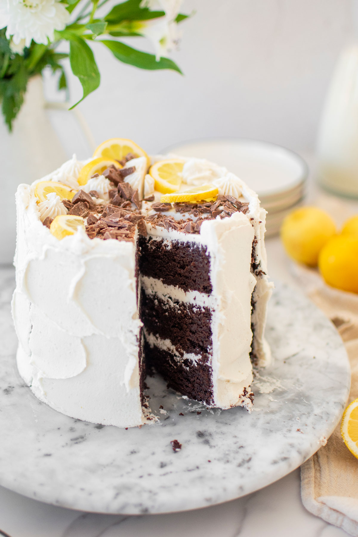 chocolate lemon layer cake with chocolate shavings and lemon slices on top sitting on a marble cake spinner cut into slices.