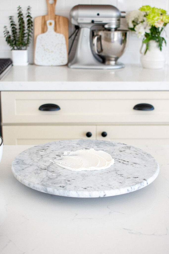 frosting spread onto a cake spinner on a white marble counter.
