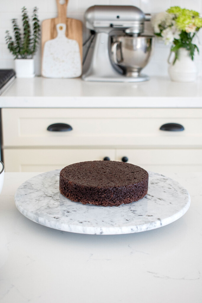 chocolate cake on a cake spinner on a white marble counter.