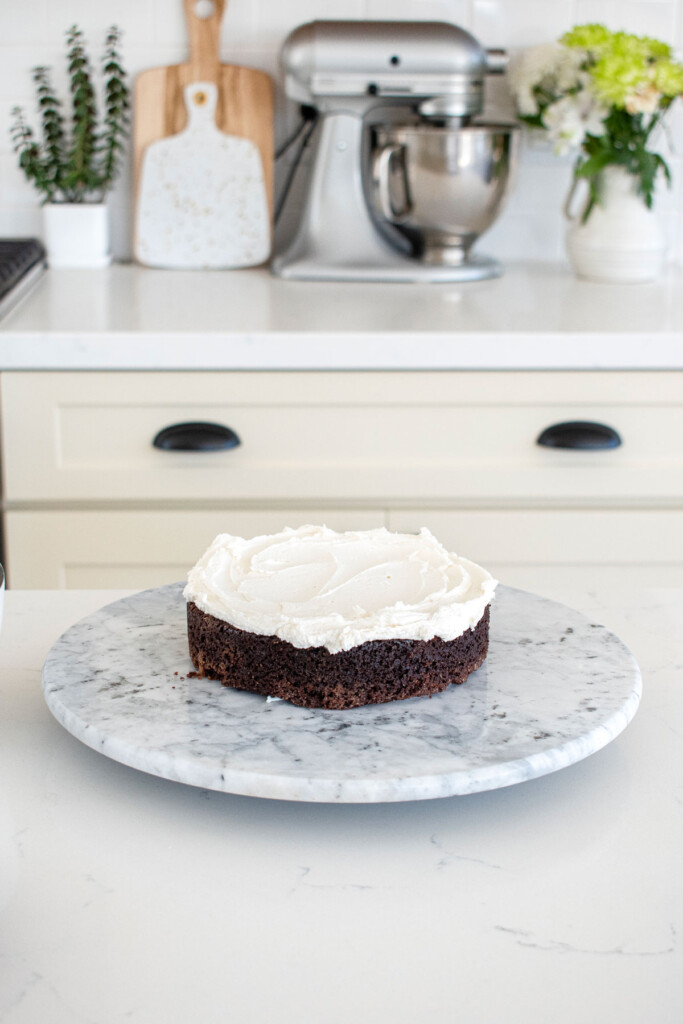 chocolate cake with vanilla frosting on a cake spinner on a white marble counter.