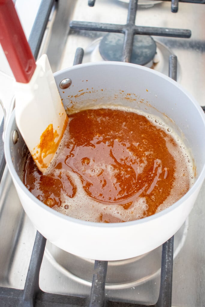 butter being stirred into melted sugar in a small pot over the stove, making homemade caramel lollipops.