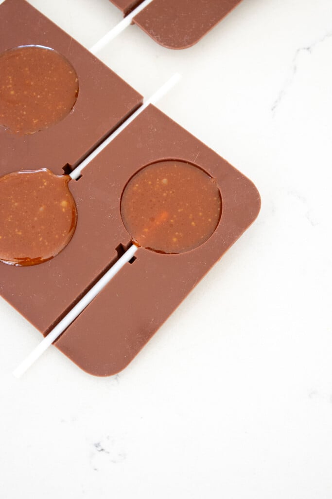 homemade caramel lollipops in a silicone mold on a white countertop.