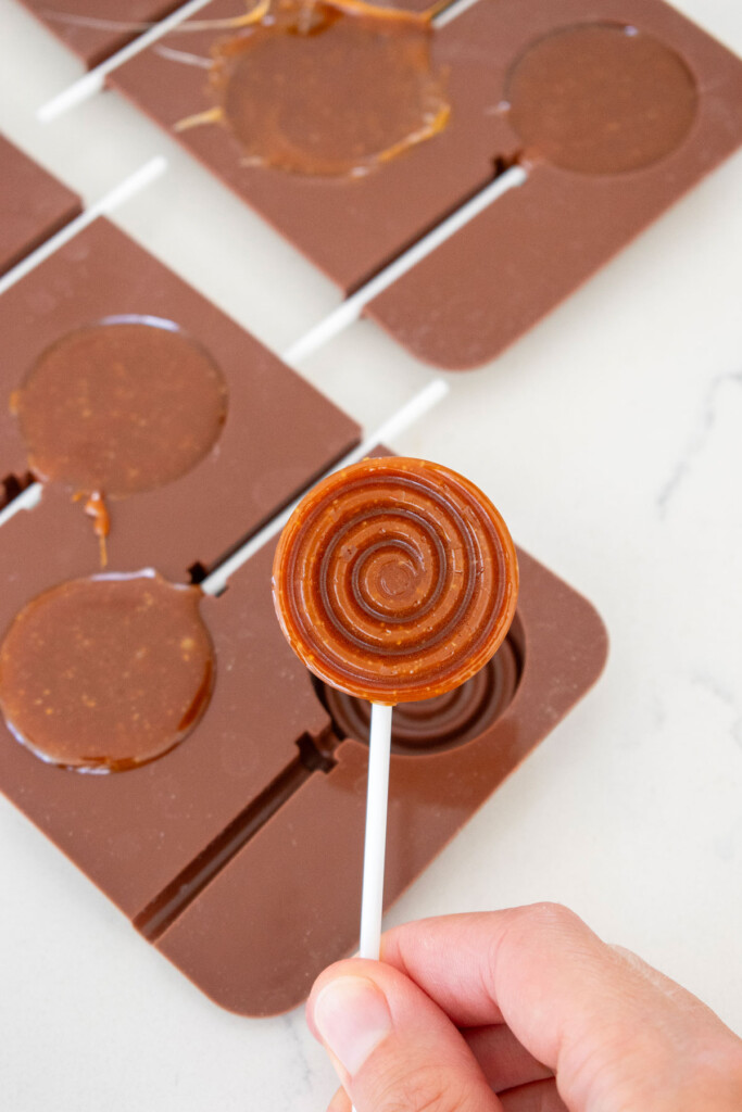removing a homemade caramel lollipop from a silicone mold on a white countertop.