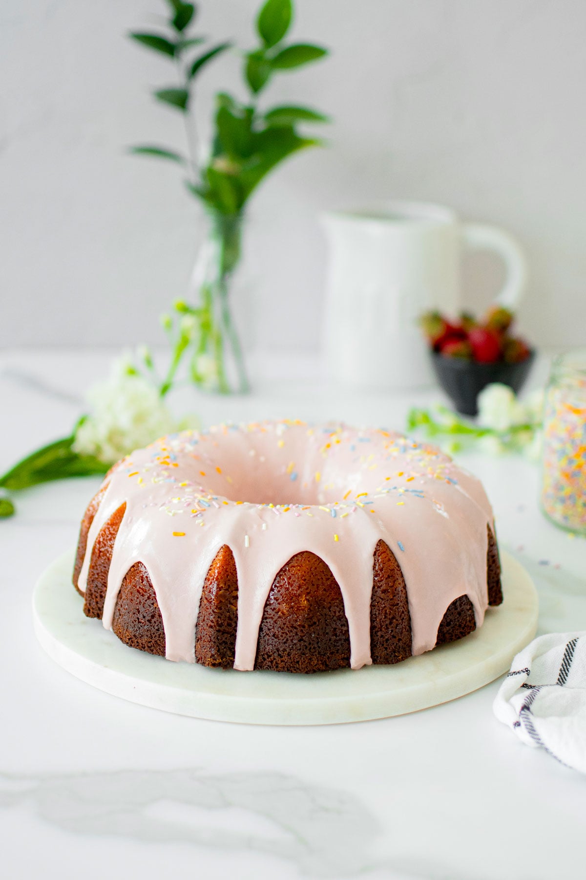 strawberry donut pound cake on a marble serving board on a white marble counter with fresh flowers.