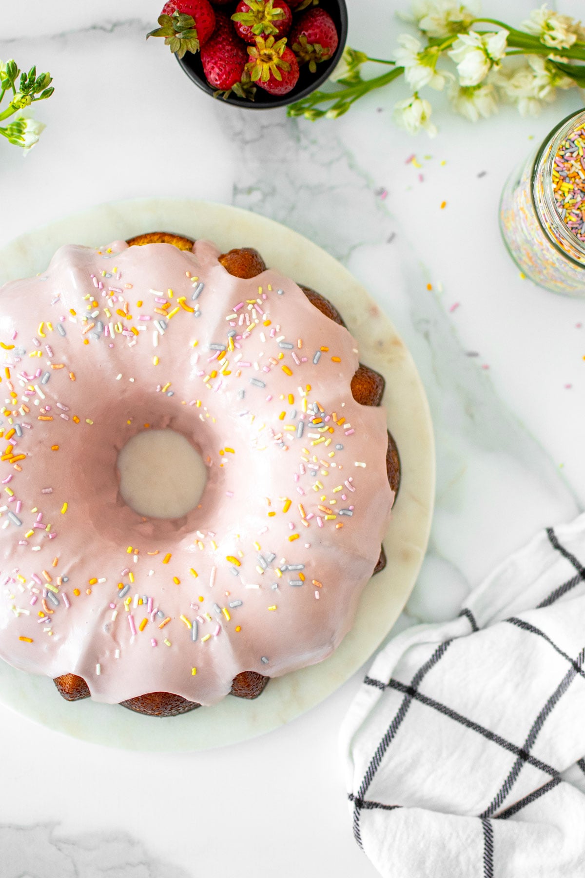 strawberry donut pound cake on a marble serving board on a white marble counter with fresh flowers.