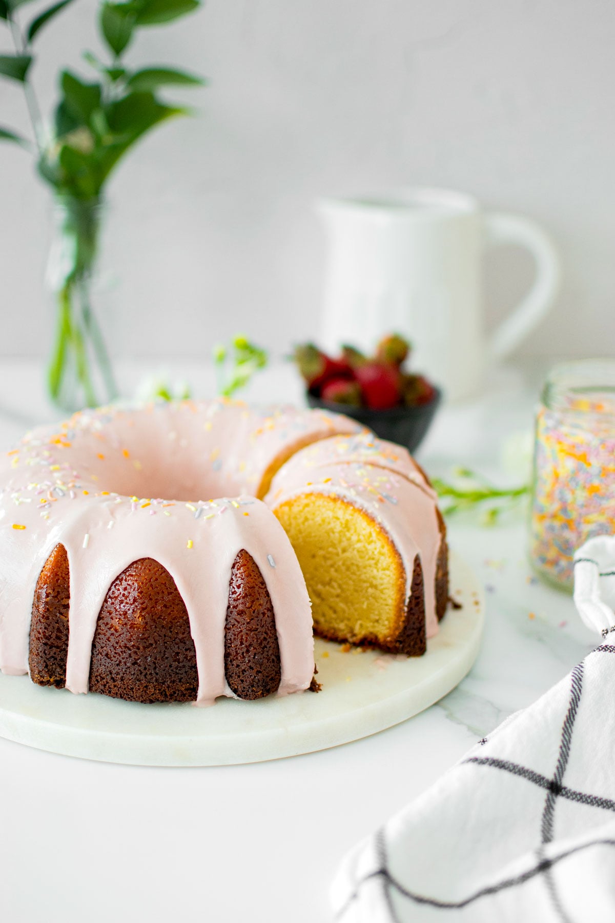 strawberry donut pound cake on a marble serving board on a white marble counter with fresh flowers.