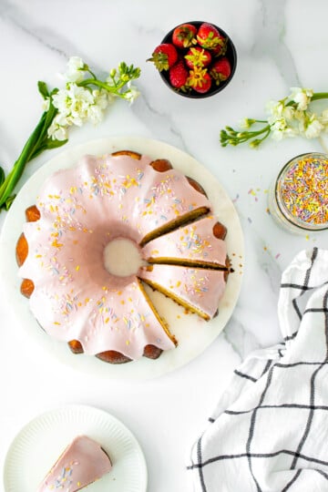strawberry donut pound cake on a marble serving board on a white marble counter with fresh flowers.