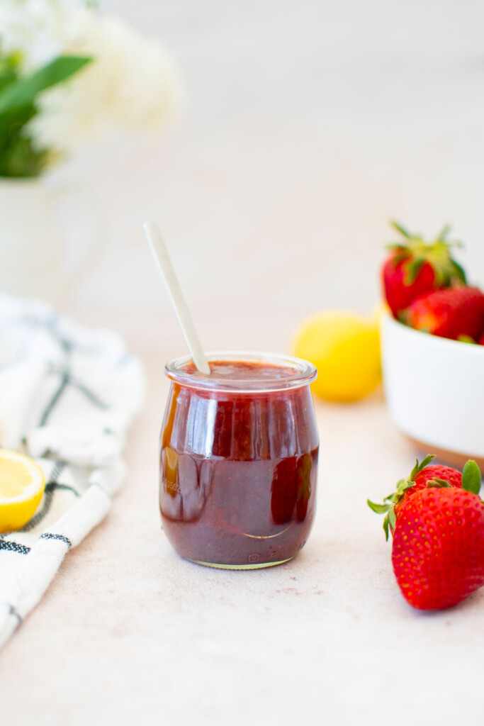 organic strawberry jam in a glass jar with a spoon with fresh strawberries and lemon.