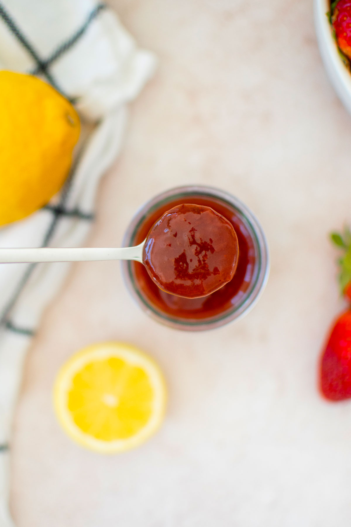 organic strawberry jam in a glass jar with a spoon and fresh lemon and strawberries.