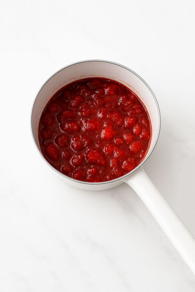 organic strawberry jam in a white pot on a marble counter.