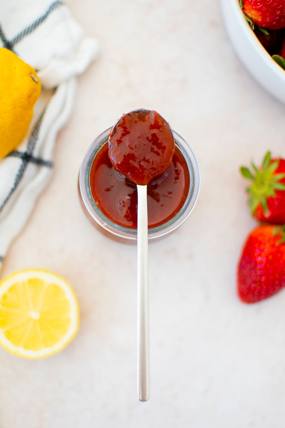organic strawberry jam in a glass jar with a spoon and fresh lemon and strawberries.