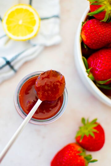organic strawberry jam in a glass jar with a spoon on a table with fresh strawberries and a lemon.