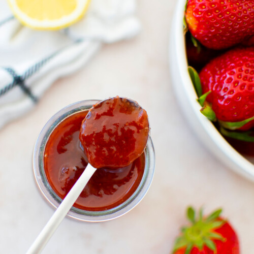 organic strawberry jam in a glass jar with a spoon and fresh lemon and strawberries.