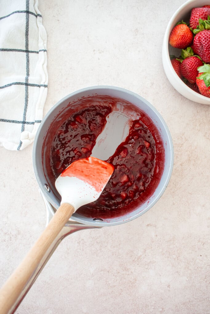 homemade strawberry jam in a small pot with a spatula being run through the middle of it.