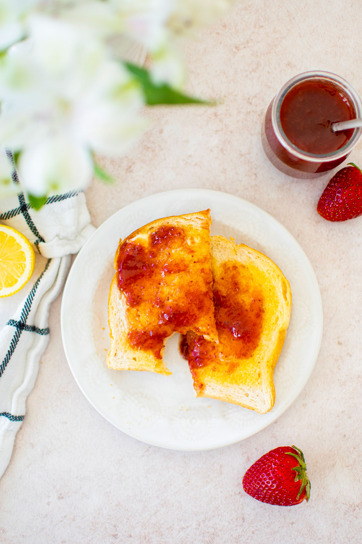 toasted sourdough bread with butter and strawberry jam sliced in half on a plate on a table with fresh flowers and a jarm jar.