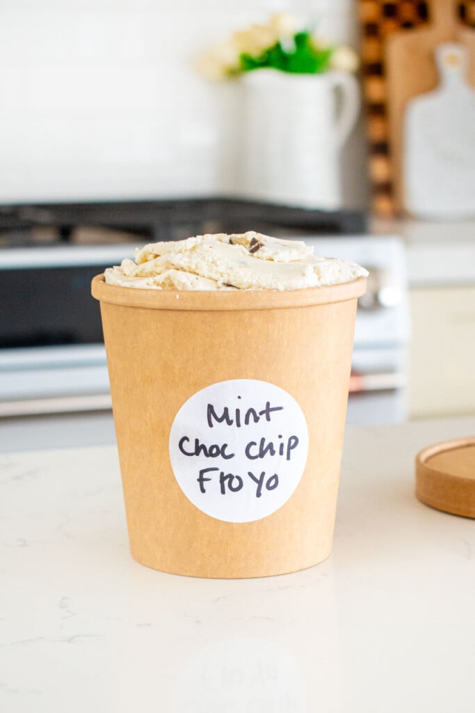 kraft container of mint chocolate chip fro yo with a sticker on the front with the name on a white marble counter.
