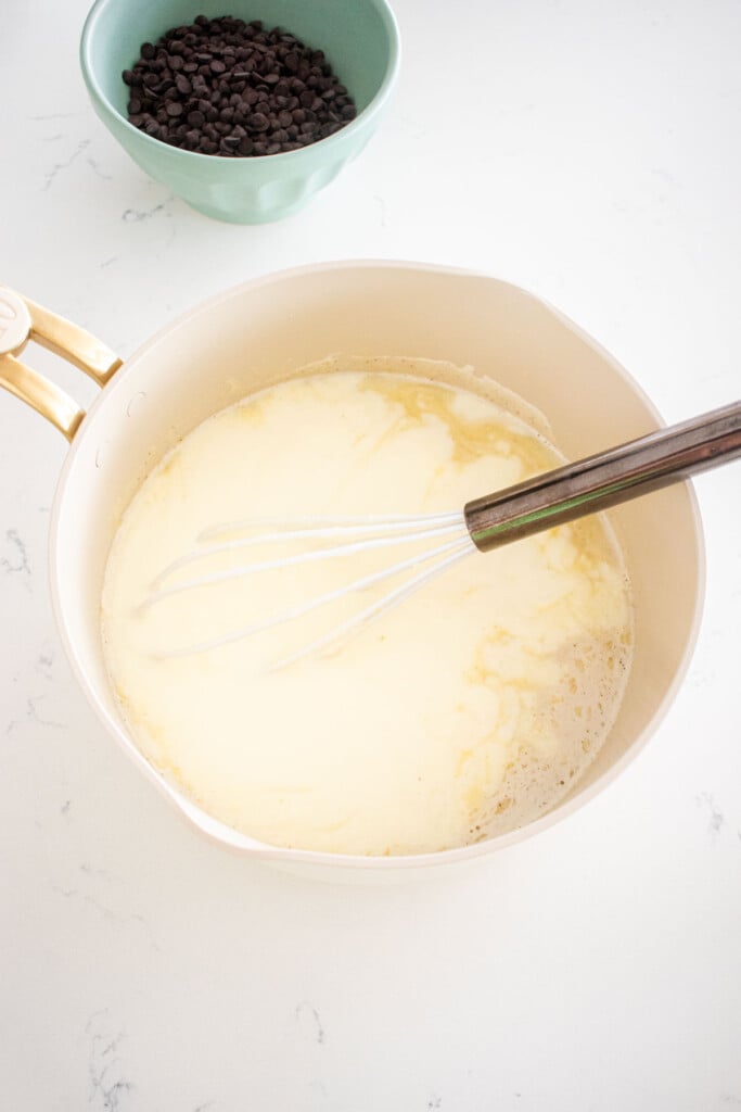 homemade mint fro yo base being whisked with yogurt in a pot on a white marble counter.