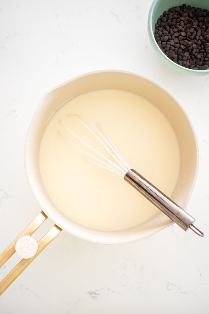 homemade mint fro yo base in a pot with a whisk on a white marble counter.