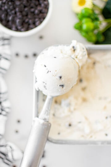 scoop of mint chocolate chip fro yo being scooped out of a pan on a white marble counter.