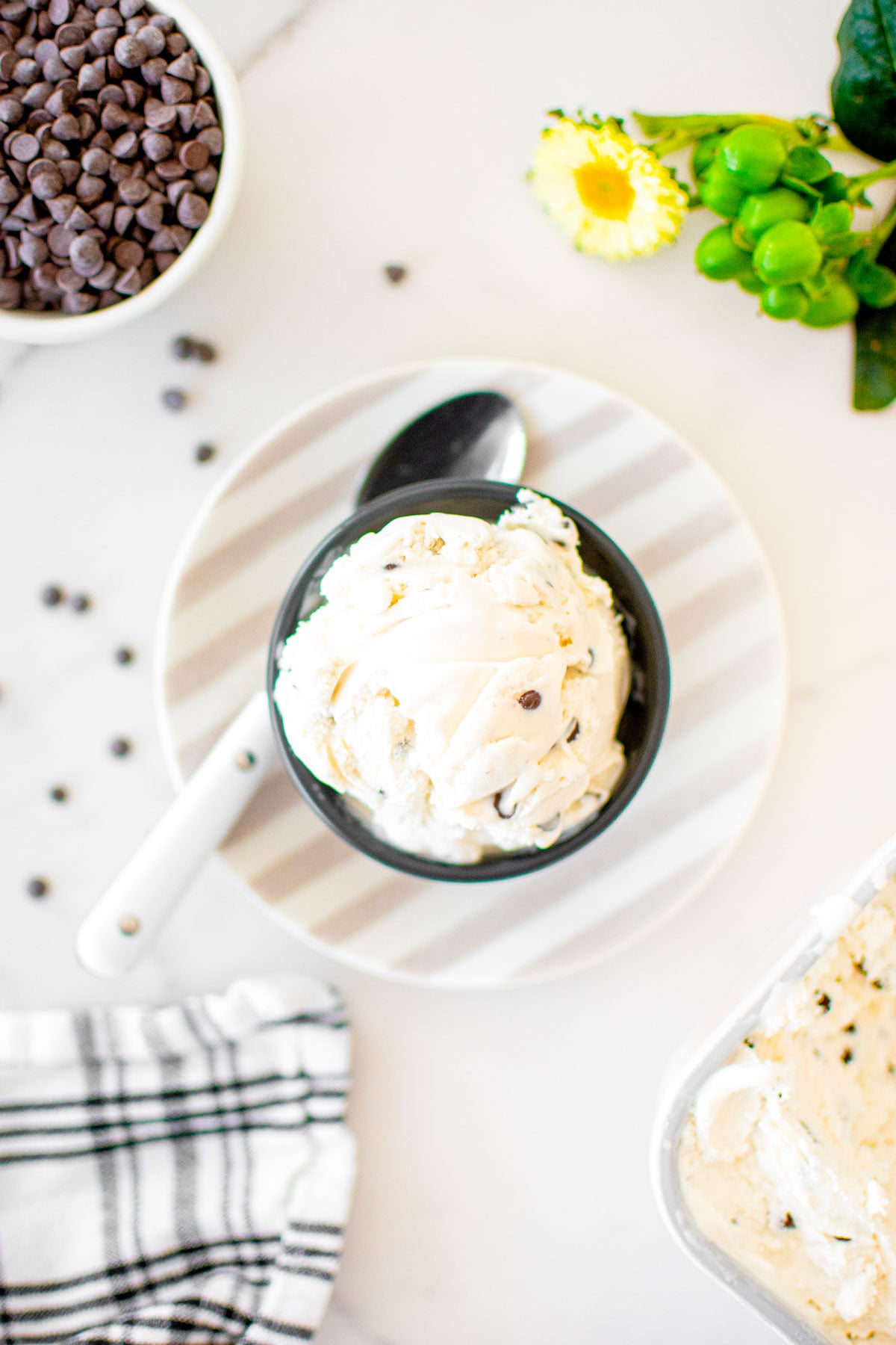bowl of homemade mint chocolate chip fro yo on a stripe plate on a marble counter with a spoon.