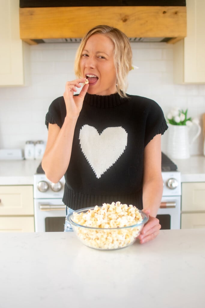 woman eating rosemary sea salt popcorn out of a glass bowl in the kitchen.
