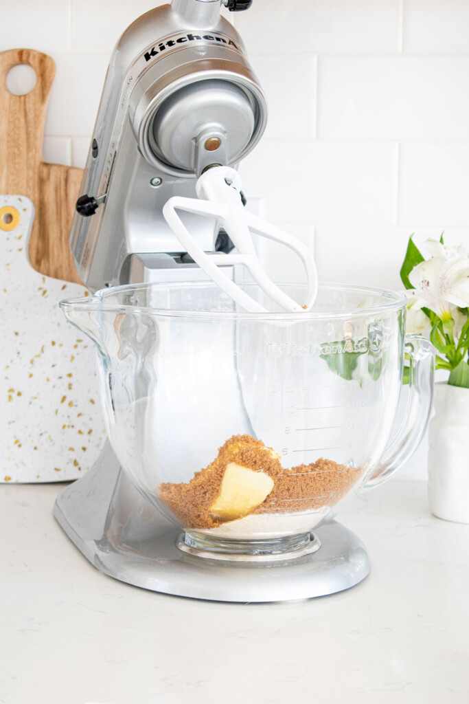 butter and sugar in a glass stand mixing bowl on a white marble counter.