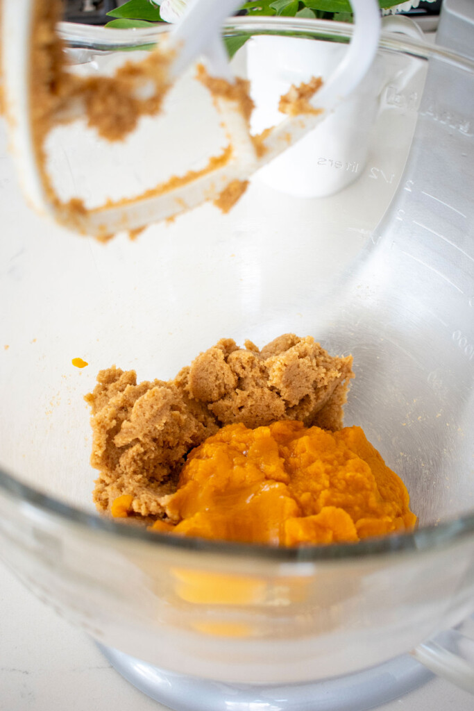 creamed butter and sugar with pumpkin in a glass mixing bowl on a white marble counter.
