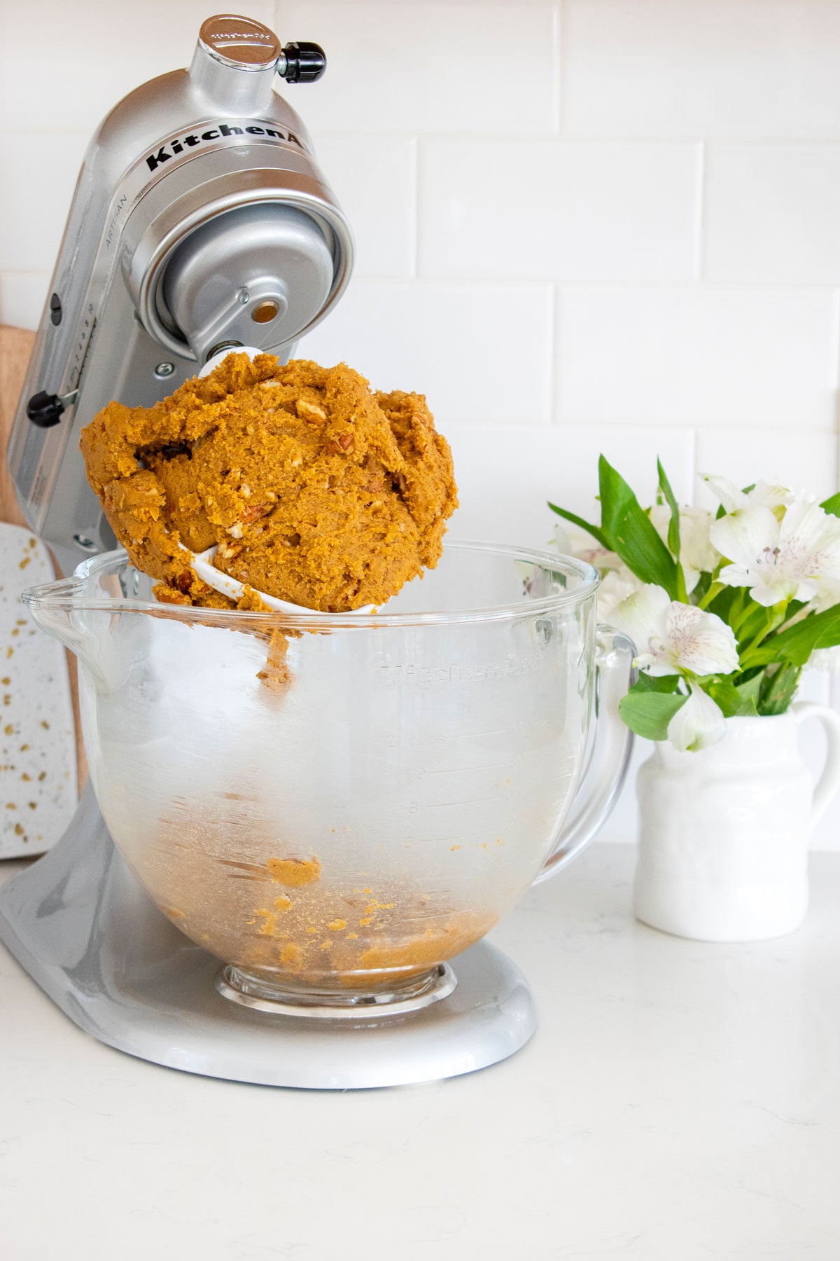 pecan pumpkin spice cookie dough in a stand mixer on a whtie marble counter.