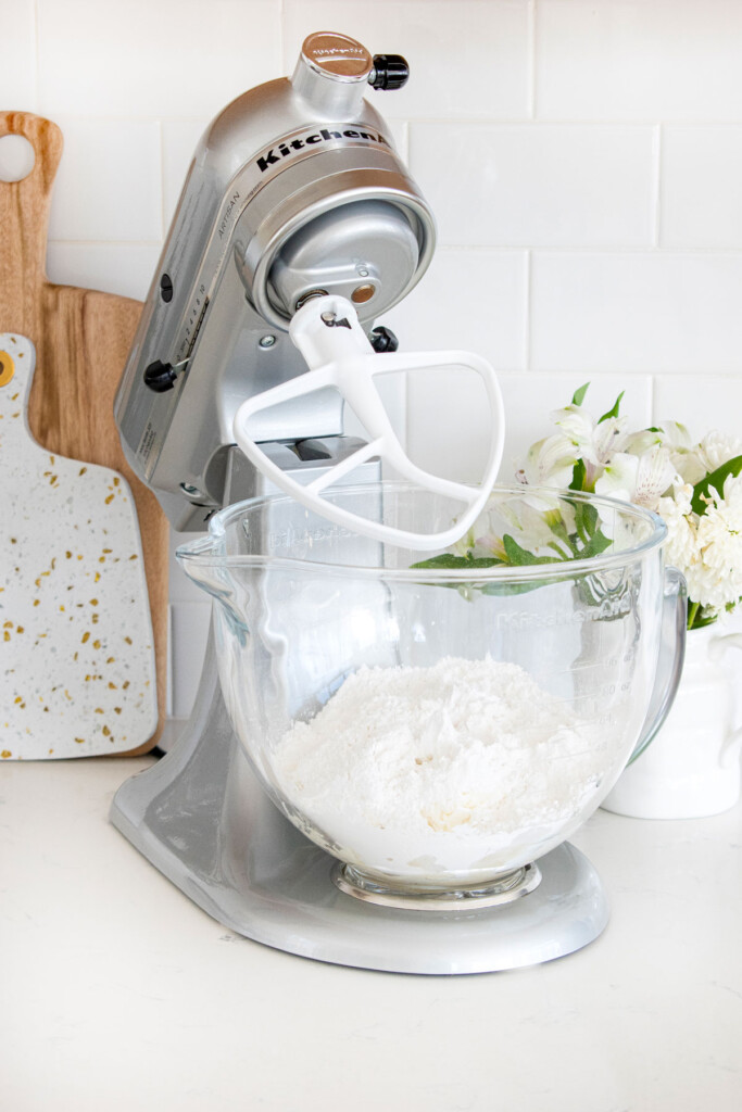 stand mixer on a white marble counter with ingredients for frosting.