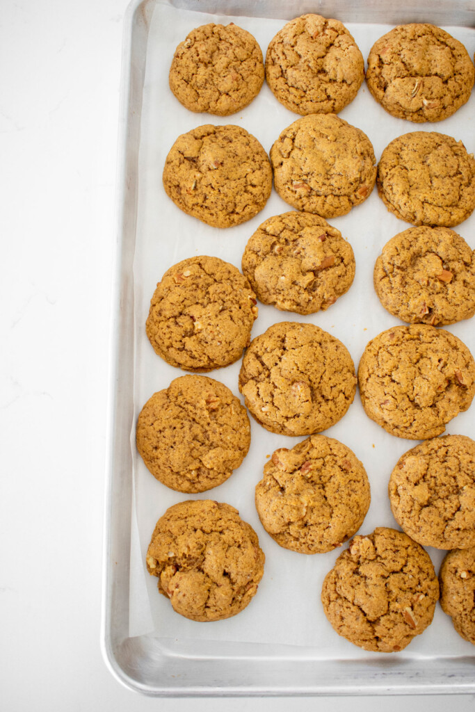 pecan pumpkin spice cookies on a baking sheet on a white marble counter.
