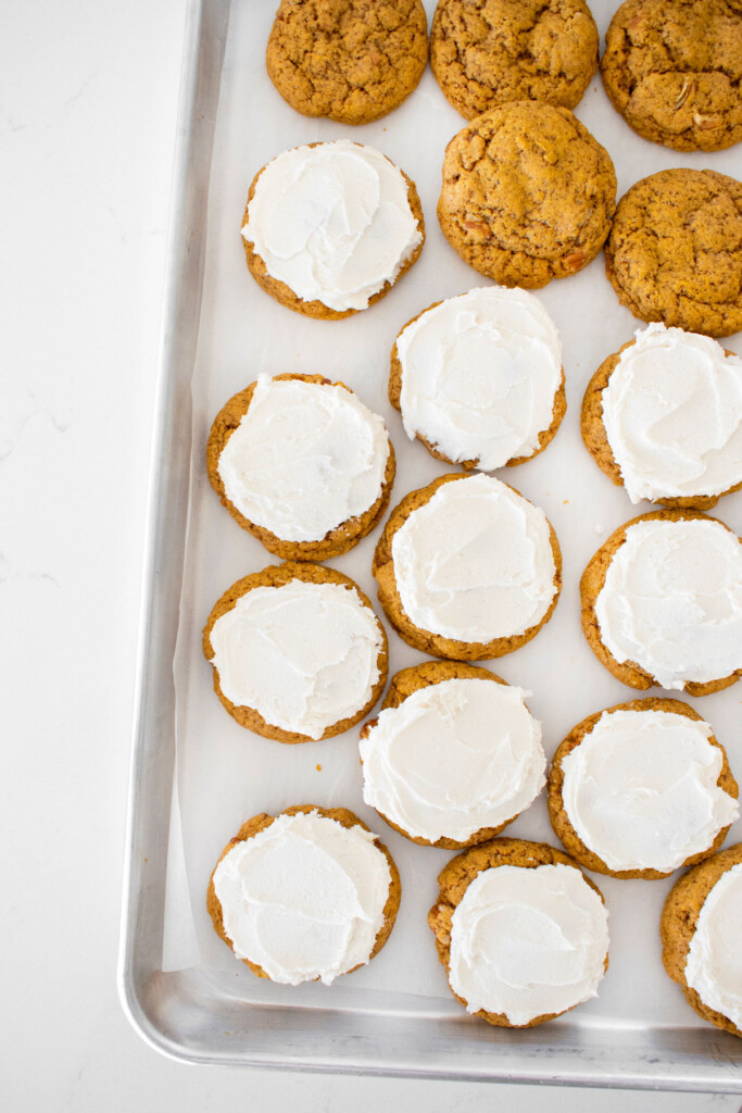 frosted pecan pumpkin spice cookies on a baking sheet on a white marble counter.