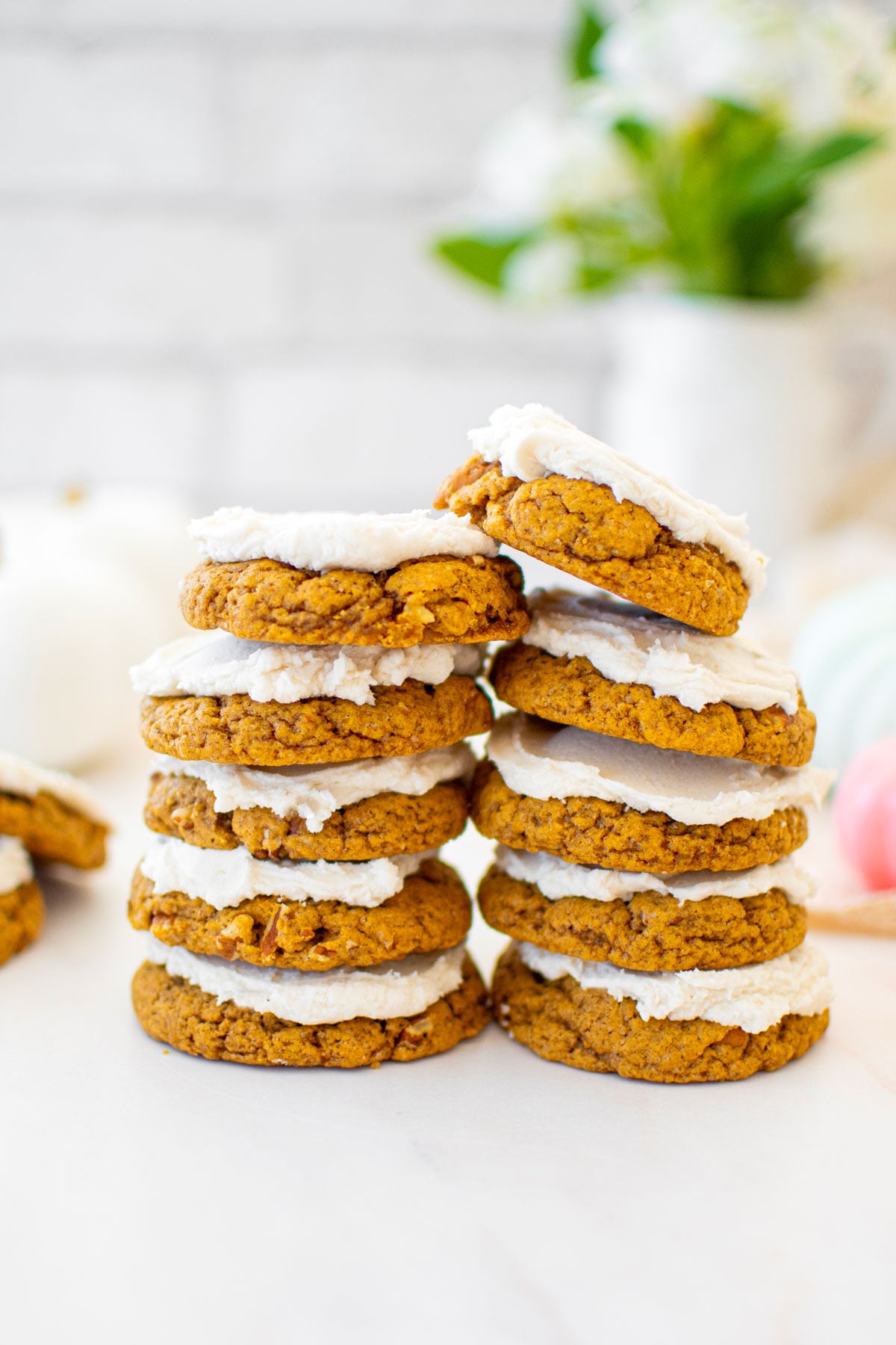 stack of frosted pecan pumpkin spice cookies on a white marble counter with fresh flowers.