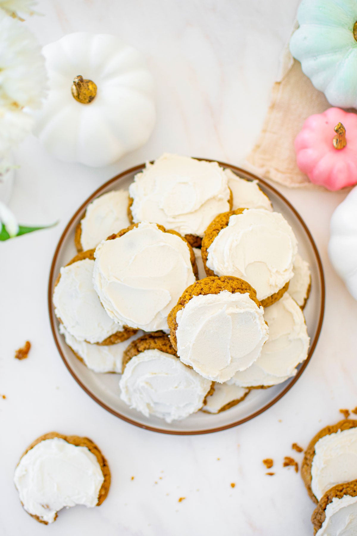plate of frosted pecan pumpkin spice cookies on a white marble counter with pumpkins.