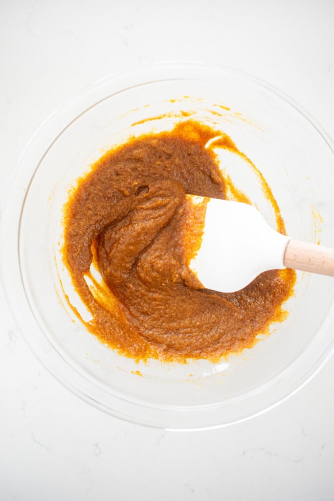 pumpkin pie pop tart filling mixed together with a spatula in a glass mixing bowl on a white marble counter.
