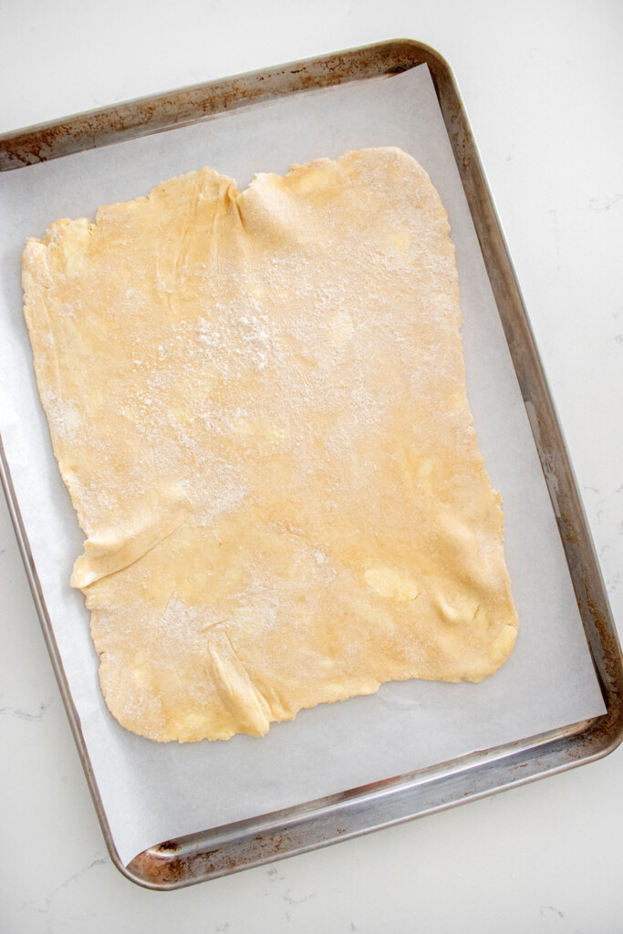 pie dough rolled into a large rectangle on a baking sheet on a marble counter.