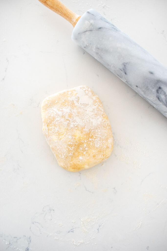 pie dough with flour sprinkled on top on a white marble counter with a marble rolling pin.