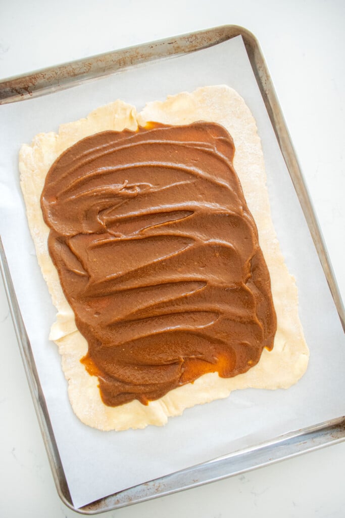 pie dough rolled out on a baking sheet and spread with pumpkin filling.