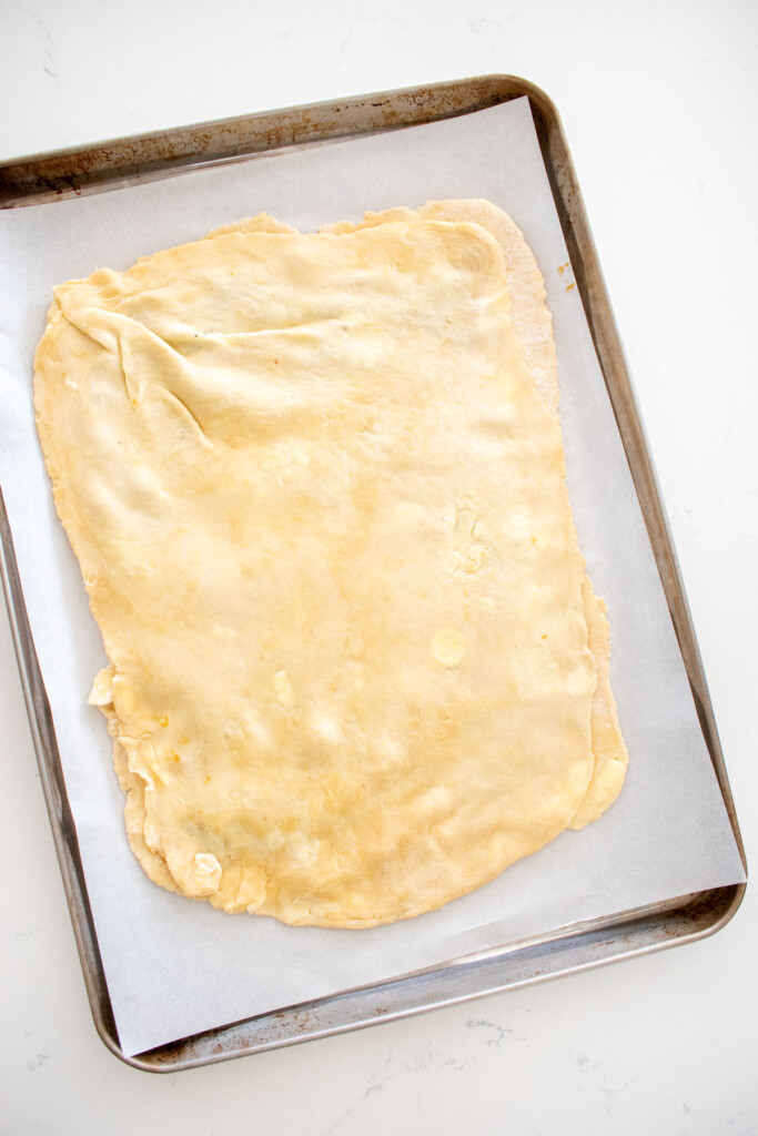 giant pumpkin spice pop tart being assembled on a baking sheet on a marble counter.