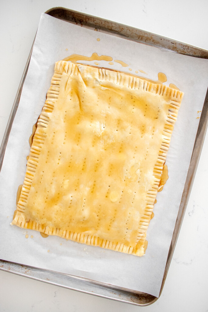 giant pumpkin spice pop tart on a baking sheet brushed with honey pie wash.