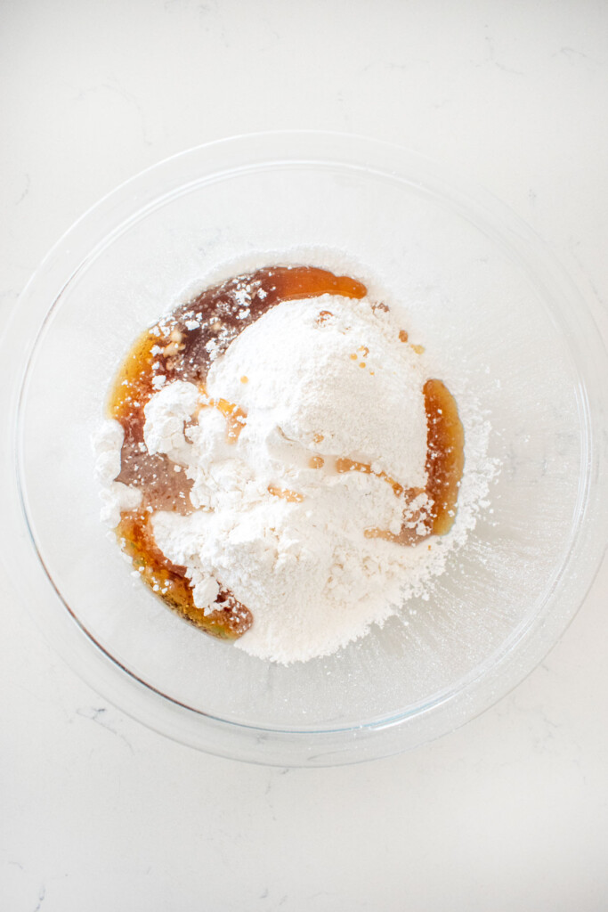 glass mixing bowl with powdered sugar and maple syrup on a white marble counter.