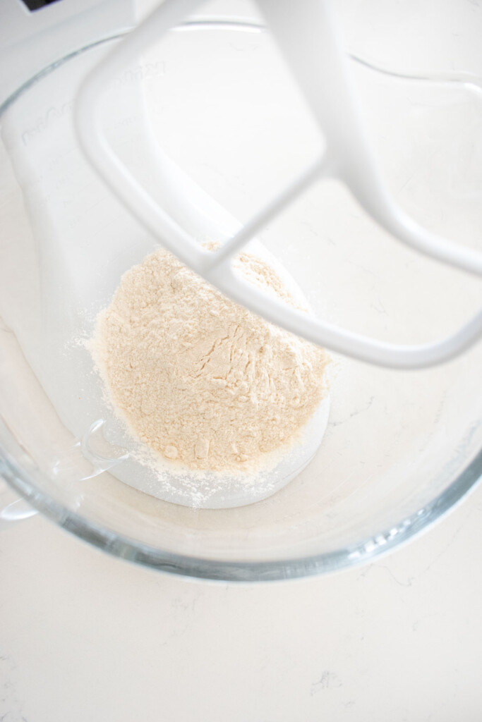 flour and sugar in a glass stand mixing bowl on a white marble counter.