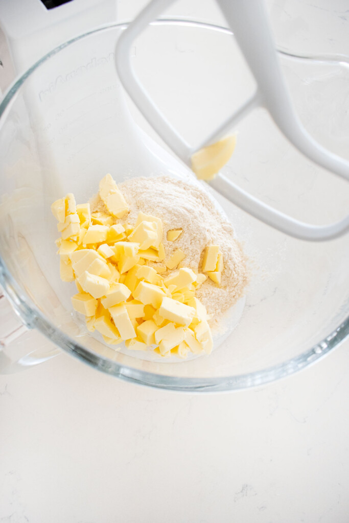 ingredients for pie dough in a glass mixing bowl on a white marble counter.
