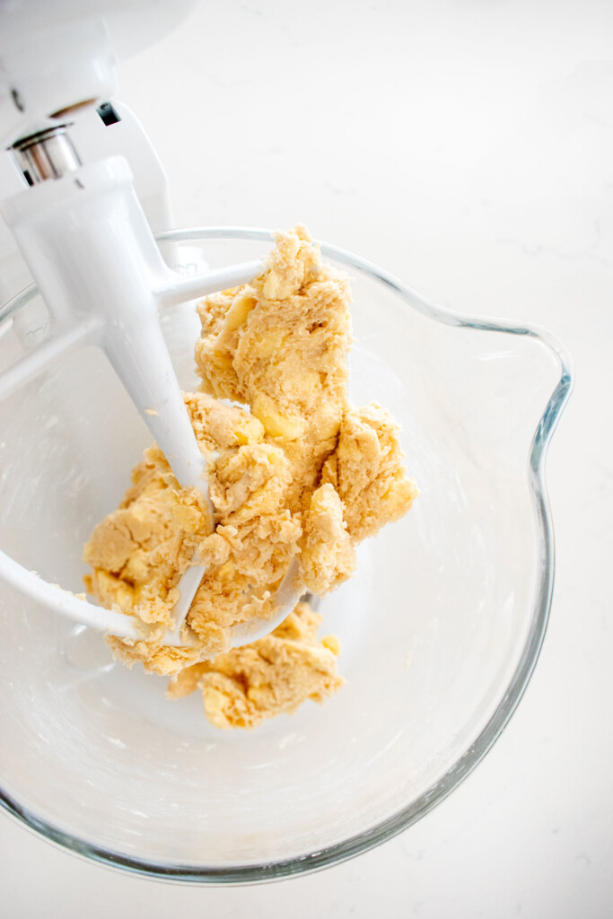 homemade pie dough in a glass mixing bowl on a white marble counter.