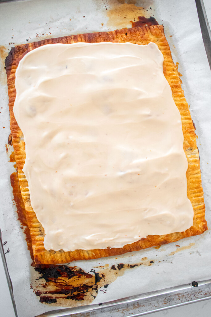 giant pumpkin spice pop tart with maple glaze on a baking sheet on a marble counter.