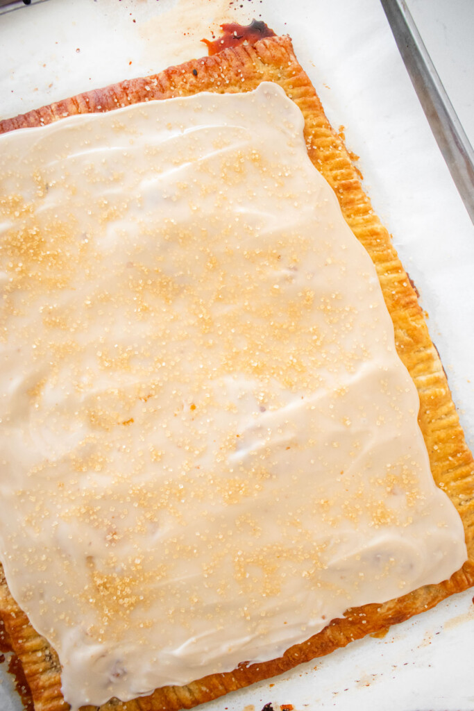 giant pumpkin spice pop tart with maple glaze and turbinado sugar on a baking sheet on a marble counter.