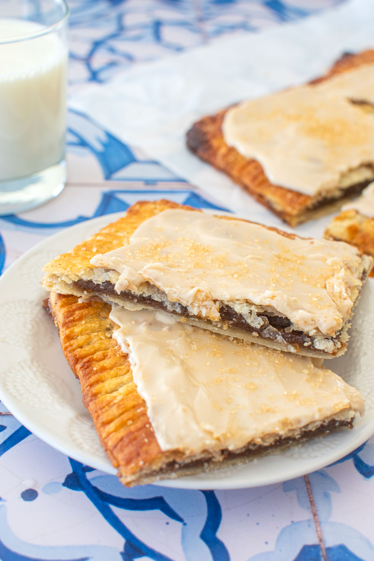 two pumpkin spice pop tarts on a plate with a glass of milk on a blue tile table.