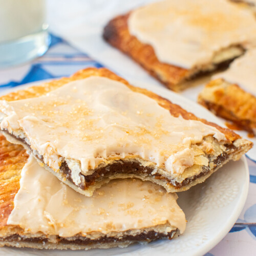 two pumpkin spice pop tarts on a plate with a glass of milk on a blue tile table.